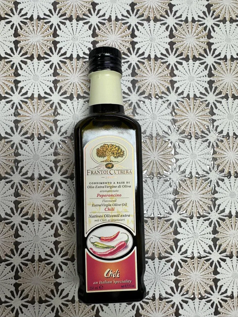 Glass cruet of golden extra virgin olive oil beside fresh olives on wood